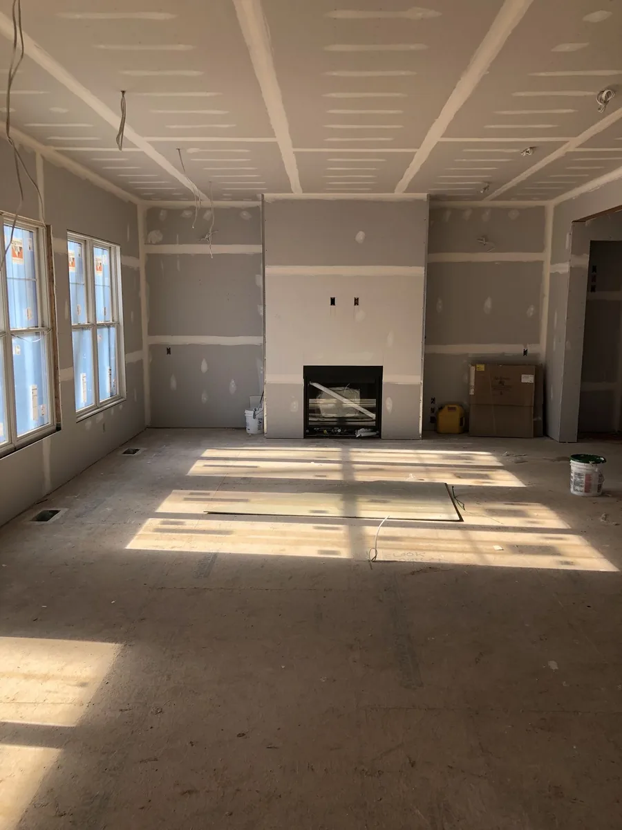 Kamer in verbouwing met onafgewerkte gipsplaatmuren, ramen links en een haard in het midden